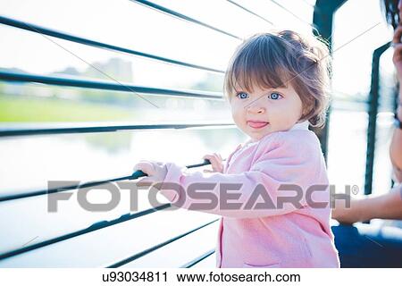 Stock Image - Cute female toddler holding riverside railings. Fotosearch