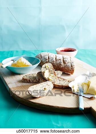 Stock Photography - Cutting board with fresh unkneaded bread with honey, butter and jam. Fotosearch