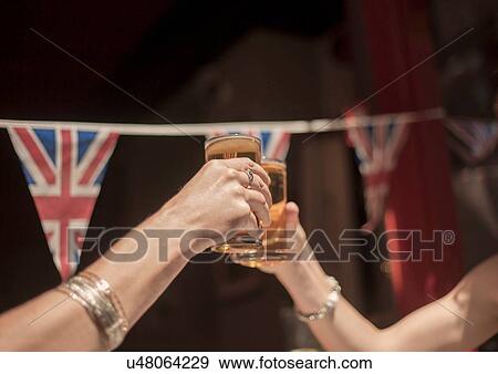 Stock Photo - Detail of two female hands raising a toast with beer outside traditional pub. Fotosearch