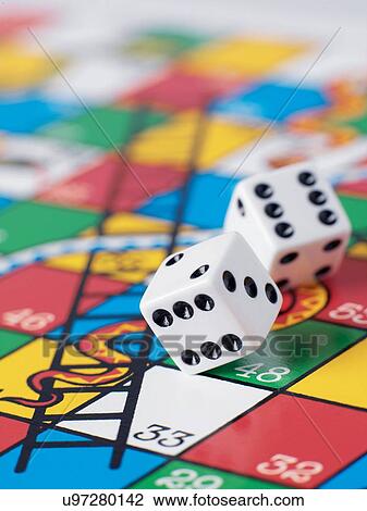 Stock Image - Dice falling onto snakes and ladders board. Fotosearch