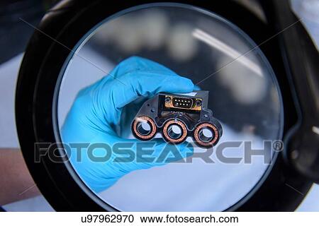 Stock Image - Electromagnets being held under magnifier on production line in electromagnetics factory. Fotosearch