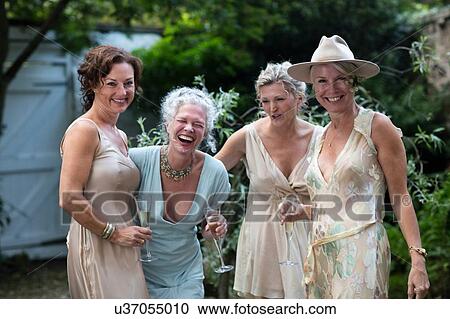 Stock Image - Elegant mature women enjoying champagne in urban garden. Fotosearch