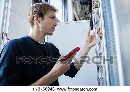 Stock Image - Factory technician using digital tablet to monitor pipes. Fotosearch