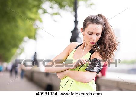 Female runner choosing music on smartphone armband at riverside View Large Photo Image Picture - Female runner choosing music on smartphone armband at riverside. Fotosearch
