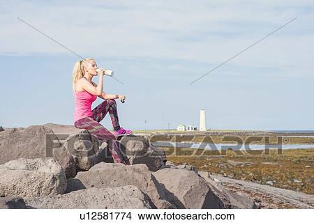 Picture - Female runner drinking from water bottle at coast. Fotosearch