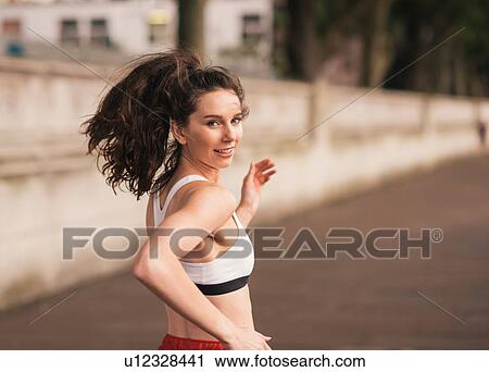 Stock Image - Female runner looking over her shoulder whilst running. Fotosearch
