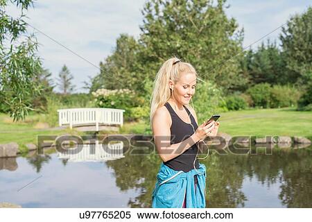 Stock Photography - Female runner selecting music for earphones in park. Fotosearch