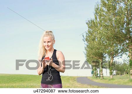 Stock Photo - Female runner selecting music on smartphone in park. Fotosearch
