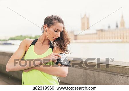 Stock Image - Female runner using smartphone touchscreen on Southbank, London, UK. Fotosearch