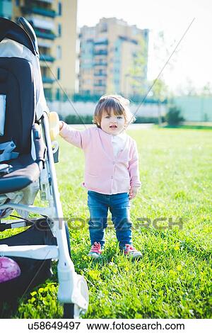 Female toddler holding onto pushchair in park View Large Photo Image Stock Photo - Female toddler holding onto pushchair in park. Fotosearch