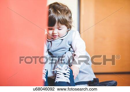 Stock Image - Female toddler playing with trainer shoes. Fotosearch