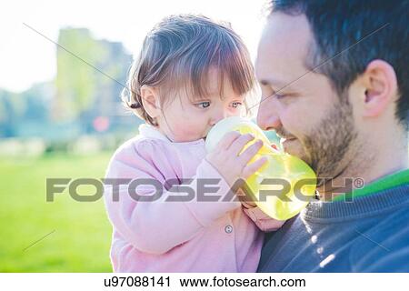 Female toddler with father drinking baby bottle in park View Large Photo Image Stock Image - Female toddler with father drinking baby bottle in park. Fotosearch