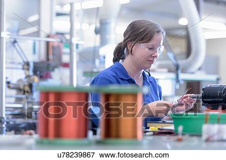 Stock Photo - Female worker assembling electromagnetic coils in electronics factory. Fotosearch