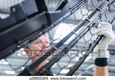 Picture - Female worker checking paint finish on automotive parts in spray paint factory. Fotosearch