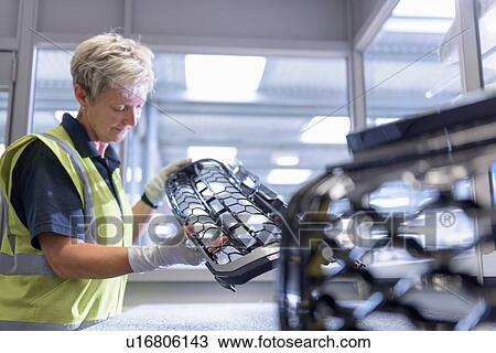 Stock Image - Female worker checking paint finish on automotive parts in spray paint factory. Fotosearch