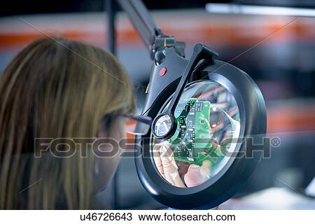 Stock Image - Female worker soldering electronic parts in clean room in electronics factory. Fotosearch