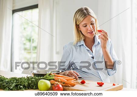 Stock Photo - Full term pregnancy young woman eating tomato slice in kitchen. Fotosearch