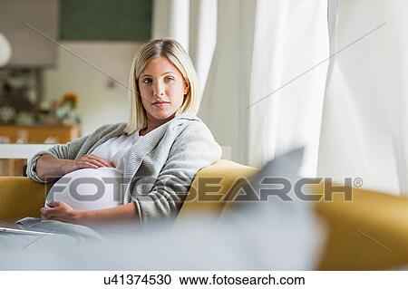 Stock Image - Full term pregnancy young woman holding stomach on sofa. Fotosearch