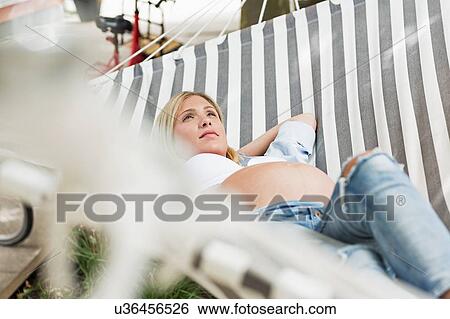 Stock Photograph - Full term pregnancy young woman lying in patio hammock. Fotosearch