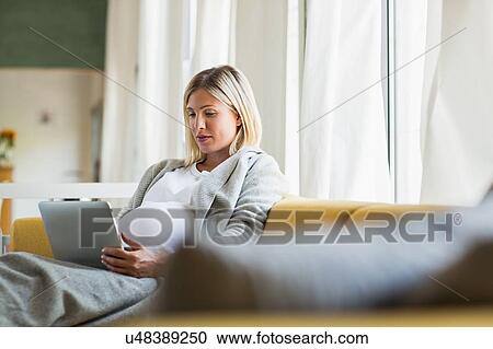 Stock Image - Full term pregnancy young woman on sofa using digital tablet. Fotosearch