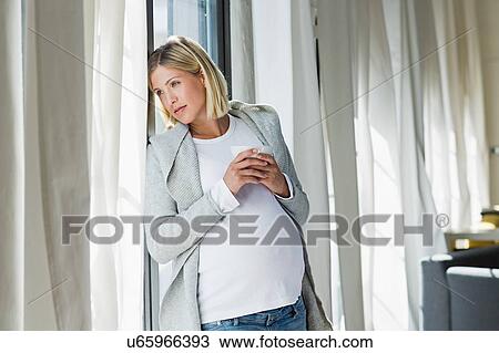Stock Image - Full term pregnancy young woman daydreaming whilst drinking coffee. Fotosearch
