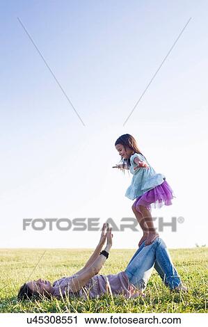 Girl balancing on top of mothers knees in park View Large Photo Image Stock Image - Girl balancing on top of mothers knees in park. Fotosearch