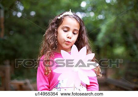 Picture - Girl blowing flower pinwheel at garden birthday party. Fotosearch