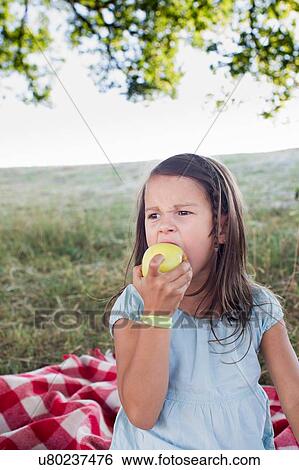 Stock Photograph - Girl eating green apple at park picnic. Fotosearch