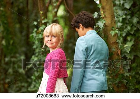 Stock Image - Girl looking over her shoulder whilst strolling with boy in garden. Fotosearch