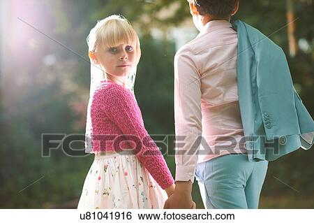Stock Photograph - Girl looking over her shoulder whilst holding boys hand in garden. Fotosearch