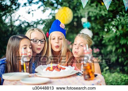 Girls blowing out candles on birthday cake at summer garden party View Large Photo Image Stock Image - Girls blowing out candles on birthday cake at summer garden party. Fotosearch