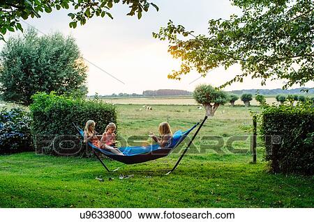 Stock Image - Girls eating on hammock at summer party, Flanders, Belgium. Fotosearch