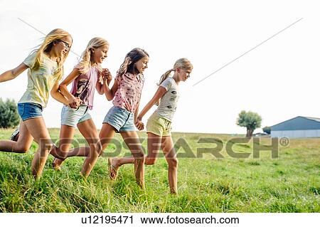 Stock Image - Girls holding hands, running in line, on field, Flanders, Belgium. Fotosearch