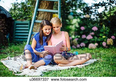 Girls reading book on grass View Large Photo Image Stock Photo - Girls reading book on grass. Fotosearch