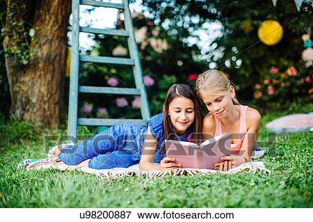 Girls reading book on grass View Large Photo Image Stock Photo - Girls reading book on grass. Fotosearch