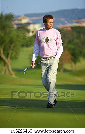 Stock Photograph - Golfer carrying golf club, hand in pocket looking away. Fotosearch