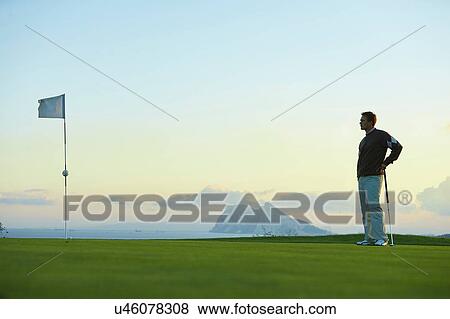 Golfer holding golf club standing near golf flag looking away View Large Photo Image Stock Photo - Golfer holding golf club standing near golf flag looking away. Fotosearch