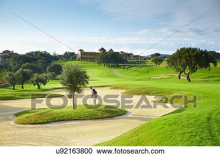 Stock Image - Golfer on island in sand trap preparing golf swing. Fotosearch