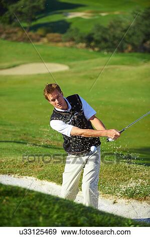 Golfer taking golf swing in sand trap, golf ball in mid air View Large Photo Image Stock Photo - Golfer taking golf swing in sand trap, golf ball in mid air. Fotosearch