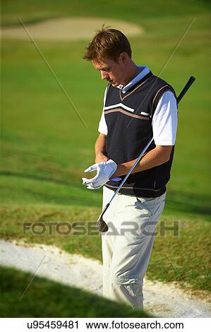 Stock Image - Golfer wearing golf glove carrying golf club under arm, looking down. Fotosearch