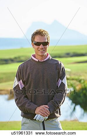 Stock Image - Golfer wearing sunglasses looking at camera smiling. Fotosearch