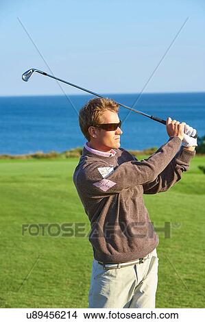 Picture - Golfer wearing sunglasses taking golf swing looking away. Fotosearch