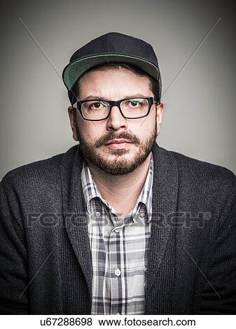 Stock Photo - Head and shoulder studio portrait of bearded young man wearing spectacles and baseball cap. Fotosearch