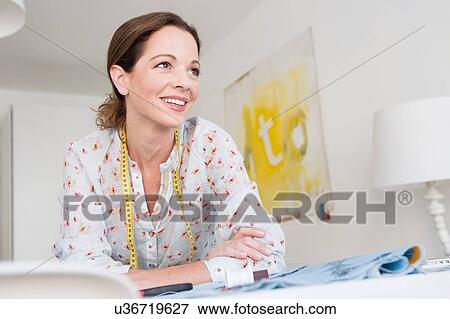 Head and shoulders of mature woman resting on elbows with tape measure looking away smiling View Large Photo Image Stock Photo - Head and shoulders of mature woman resting on elbows with tape measure looking away smiling. Fotosearch