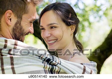 Stock Image - Head and shoulders of young couple wrapped in blanket face to face smiling. Fotosearch