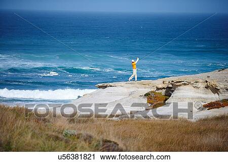 Stock Image - High angle view of golfer standing on cliff overlooking ocean taking golf swing. Fotosearch