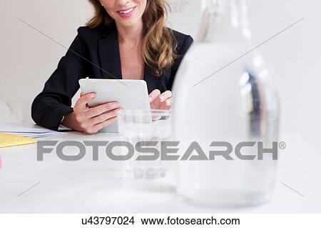 Picture - Jug and glass of water with mature woman using digital tablet. Fotosearch