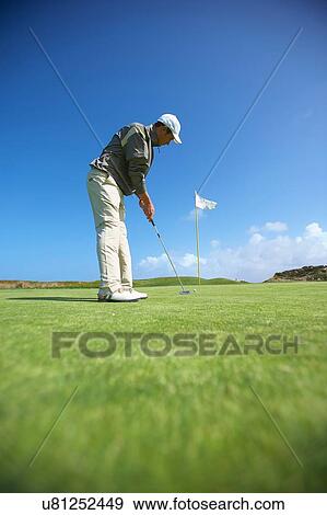 Stock Photo - Low angle full length side view of golfer putting. Fotosearch