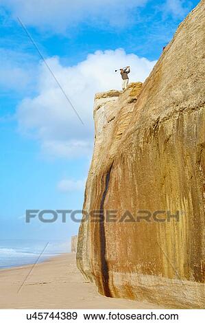 Stock Photo - Low angle view of golder on cliff top overlooking beach taking golf swing. Fotosearch