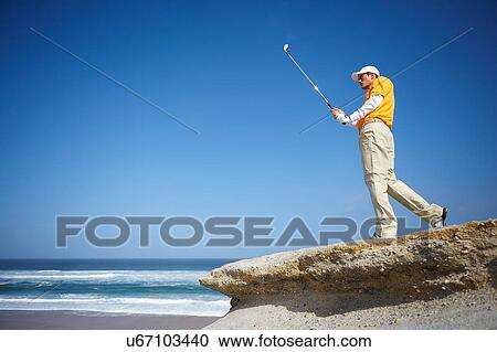 Low angle view of golfer standing on cliff overlooking ocean holding golf club View Large Photo Image Stock Image - Low angle view of golfer standing on cliff overlooking ocean holding golf club. Fotosearch